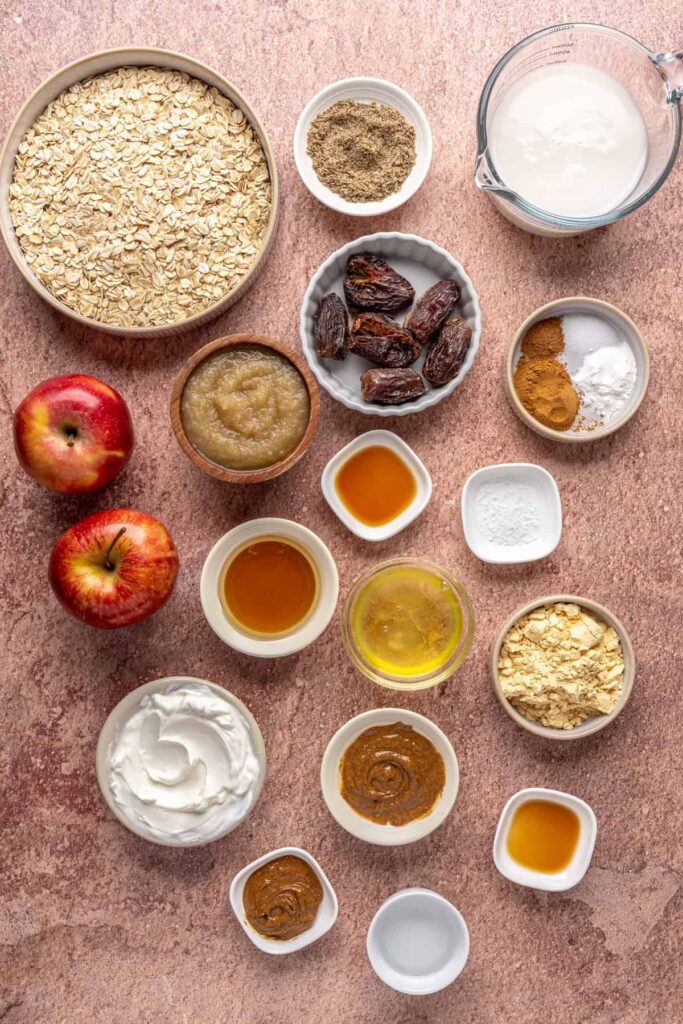 Overhead view of ingredients for baked apple oatmeal: oats, grated apples, almond milk, eggs, cinnamon, and date caramel