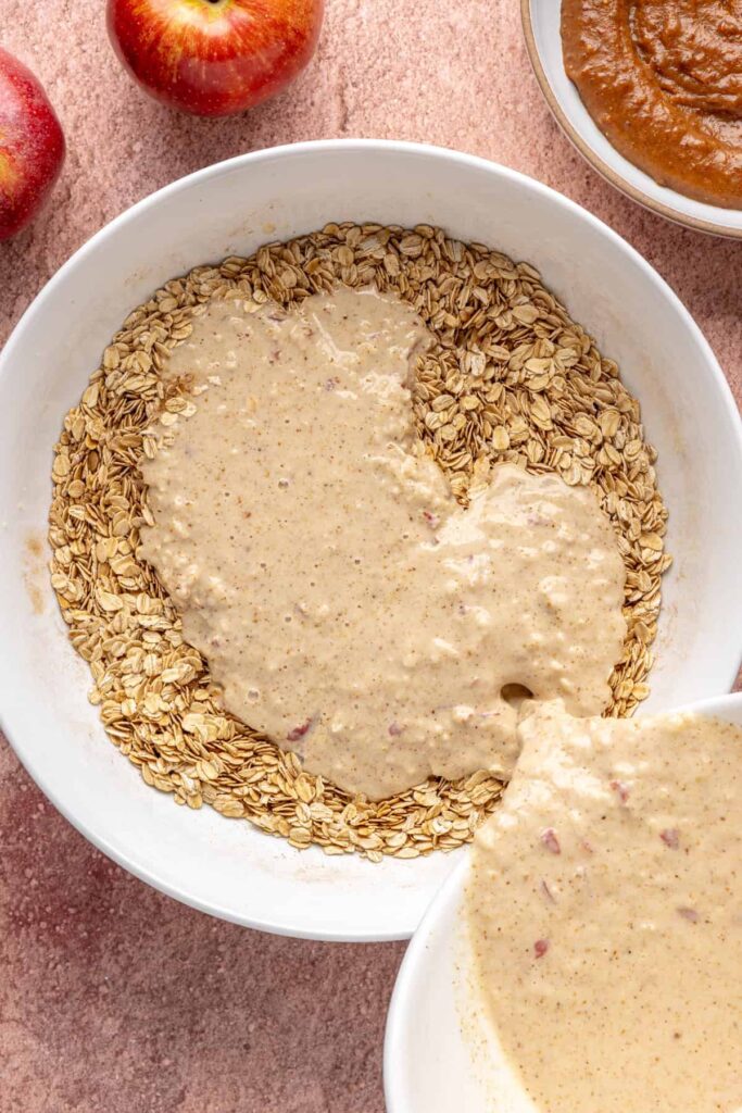 Pouring almond milk, applesauce, eggs, and nut butter into dry ingredients for baked apple oatmeal