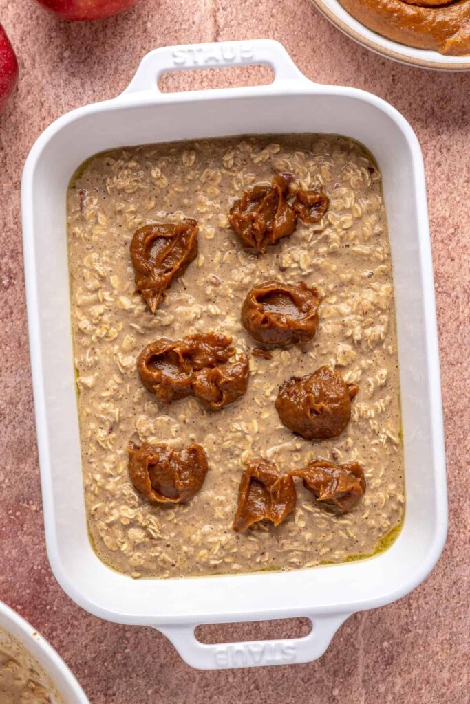 High-protein oatmeal batter for baked apple oatmeal in a baking dish with dollops of date caramel