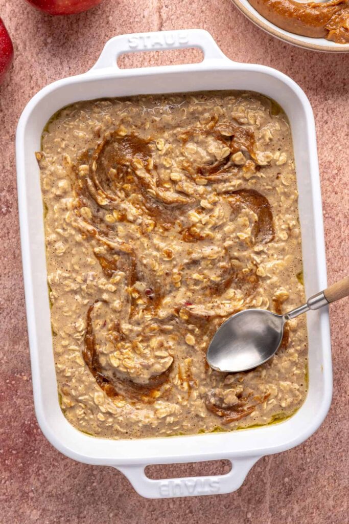 Baked apple oatmeal with caramel swirled throughout, ready to bake in a baking dish
