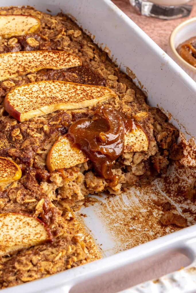 Side view of baked apple oatmeal in baking dish, caramel and apples on top