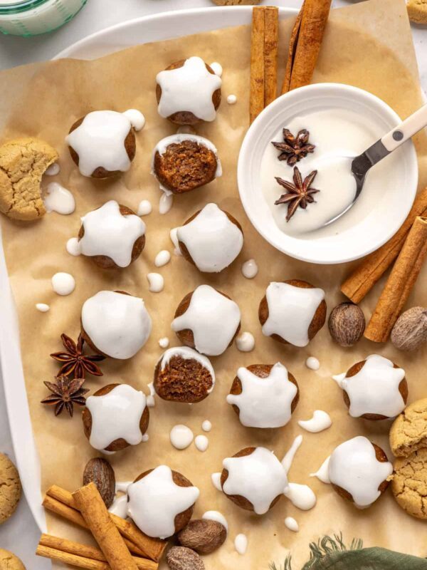 Finished gingerbread protein balls drizzled with coconut butter, styled on a baking sheet with cloves and ginger cookies, ready to enjoy