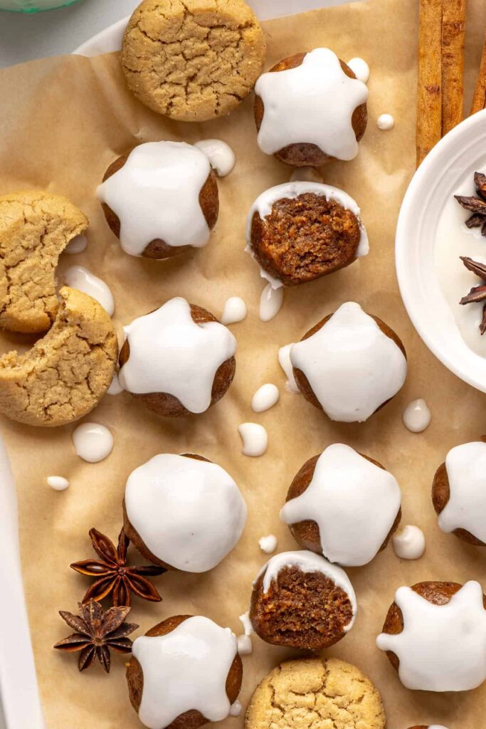Finished gingerbread protein balls drizzled with coconut butter, styled on a baking sheet with cloves and ginger cookies, ready to enjoy