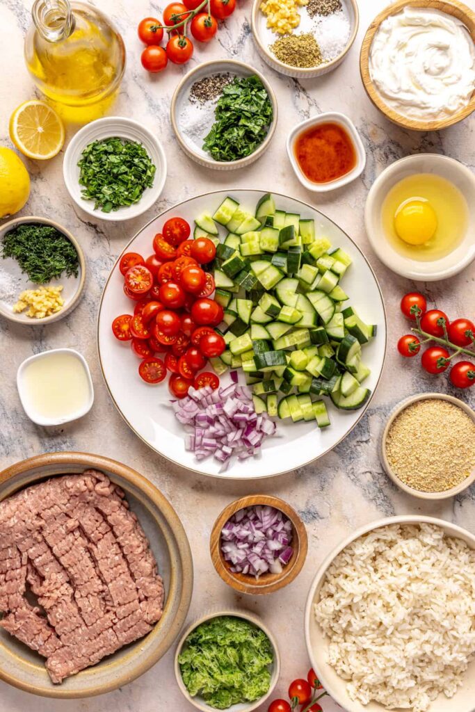 Ingredients for Greek turkey meatballs with cucumber salad and tzatziki arranged on a countertop.