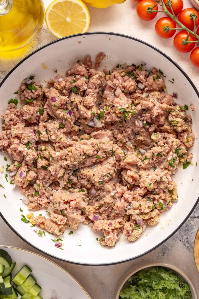 Ground turkey meatball mixture with herbs, garlic, and breadcrumbs in a bowl for Greek turkey meatballs.