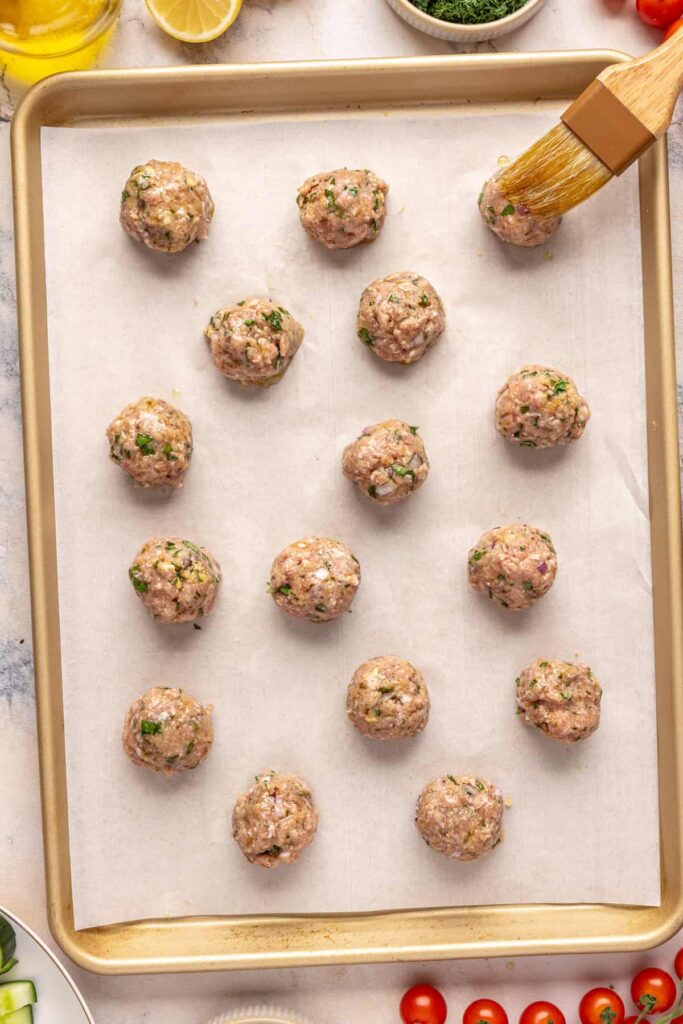 Hand-formed Greek turkey meatballs before baking, rolled and ready on a parchment-lined sheet, brushed with olive oil