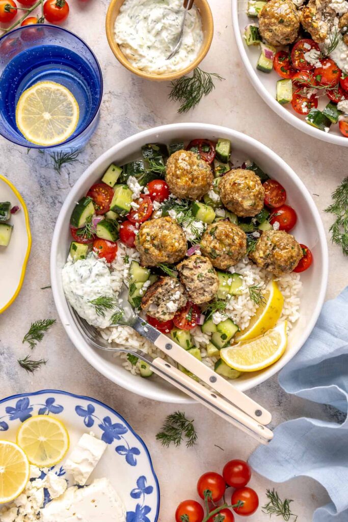 Greek turkey meatball bowl with rice, cucumber salad, and tzatziki.