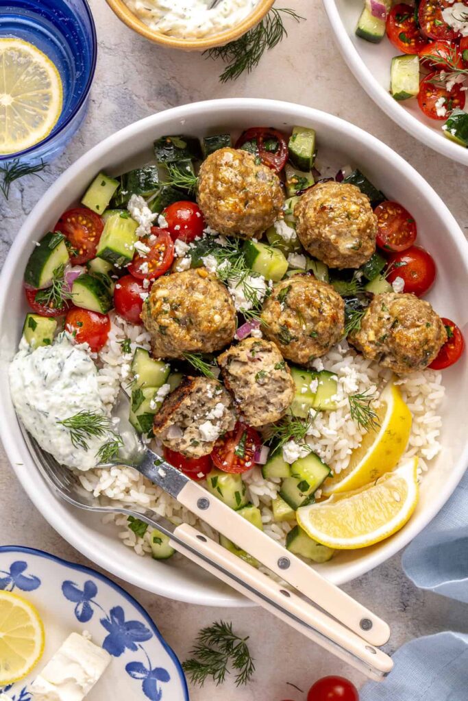Greek turkey meatball bowl with rice, cucumber salad, and tzatziki.
