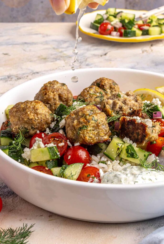 squeezing fresh lemon juice over juicy Greek turkey meatballs served over rice with tzatziki and cucumber-tomato salad.