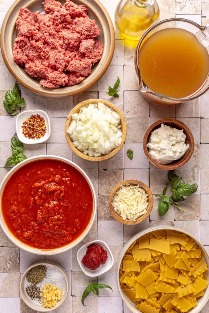 Ingredients for lasagna soup including ground beef, marinara, lasagna noodles, broth, ricotta, and herbs
