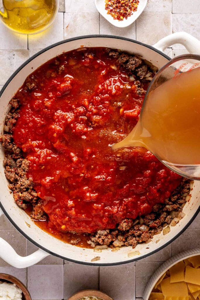 pouring bone broth and marinara sauce into the sauté pan for one pot lasagna soup
