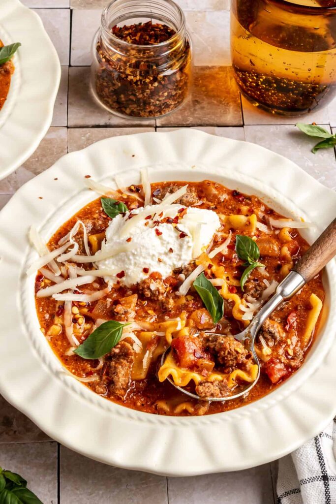High-protein lasagna soup in a bowl topped with dairy-free ricotta, basil, and chili flakes