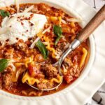 High-protein lasagna soup in a bowl topped with dairy-free ricotta, basil, and chili flakes