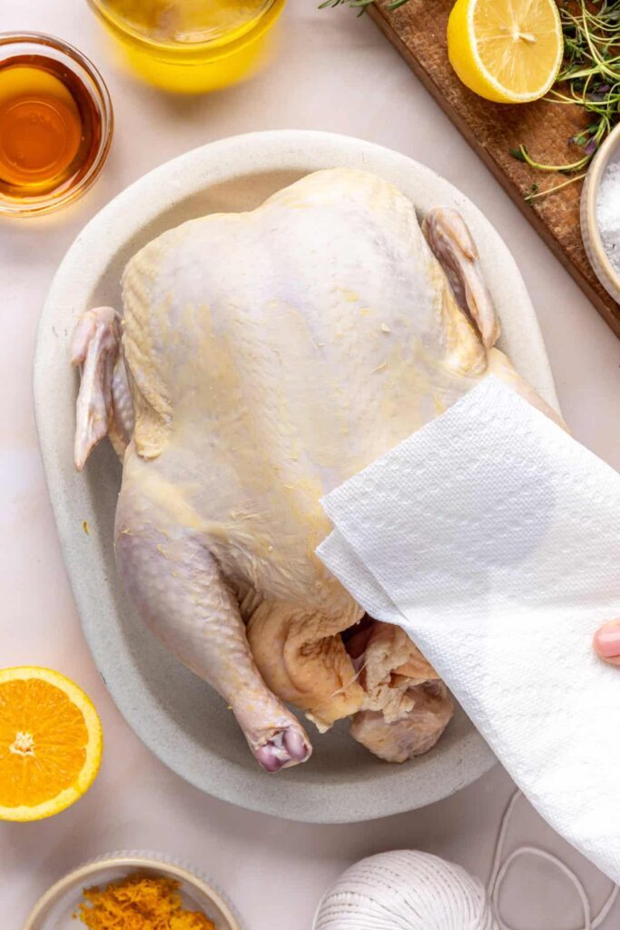 patting a whole chicken dry before brushing with Citrus Maple Glaze