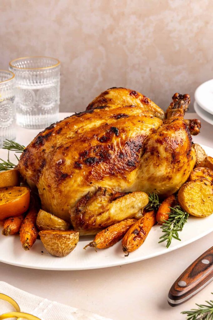 side view of Citrus Maple Chicken served on a plate with roasted carrots, potatoes, and fresh herbs