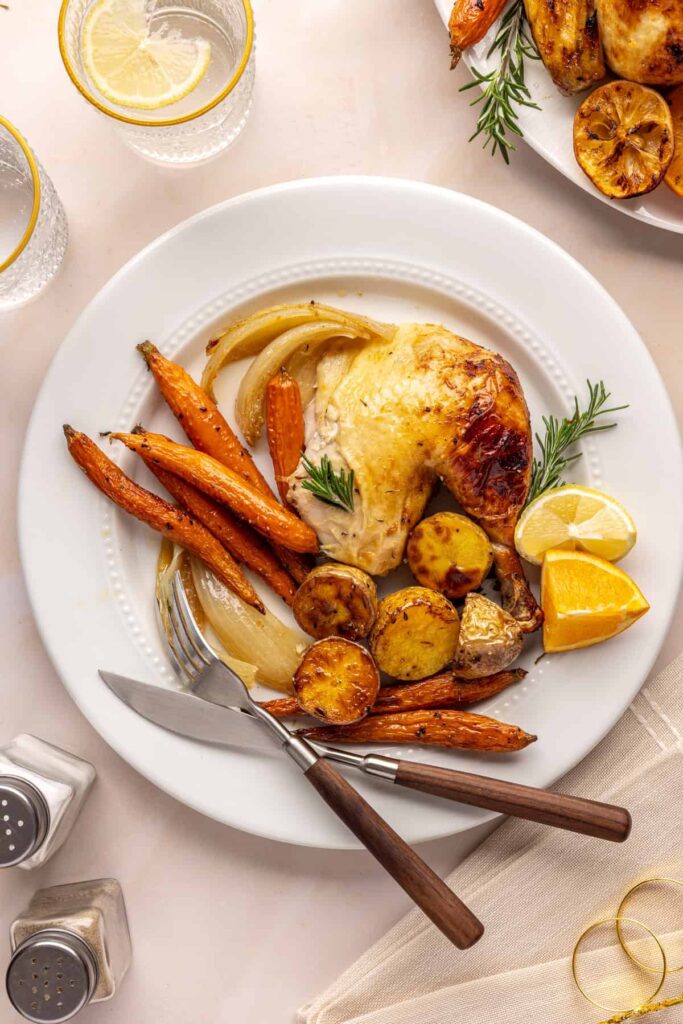 Citrus Maple Chicken with golden crispy skin served on a white plate with fresh herbs, carrots and potatoes