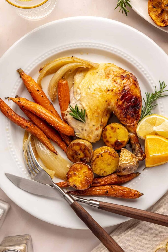 Citrus Maple Chicken with golden crispy skin served on a white plate with fresh herbs, carrots and potatoes