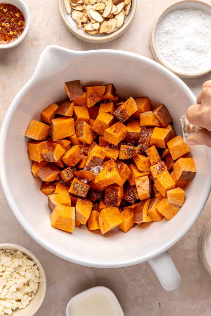 drizzling olive oil over sweet potato cubes in a bowl before roasting