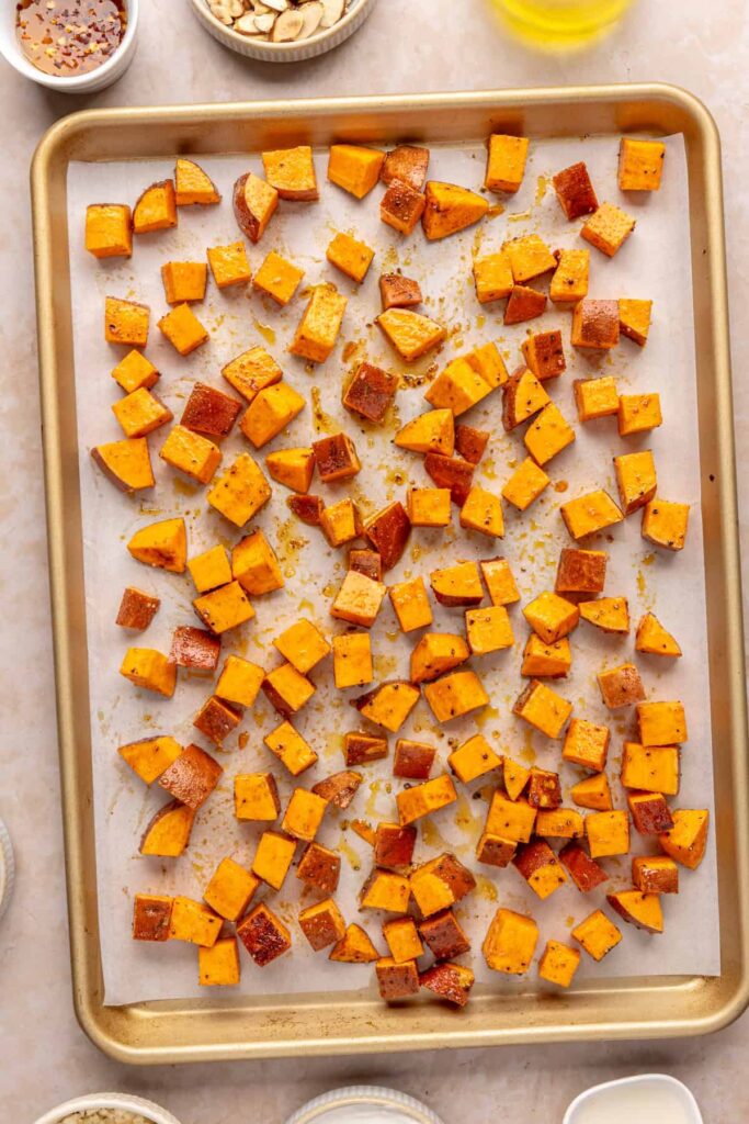 Sweet potatoes roasting on a parchment-lined baking sheet until golden brown