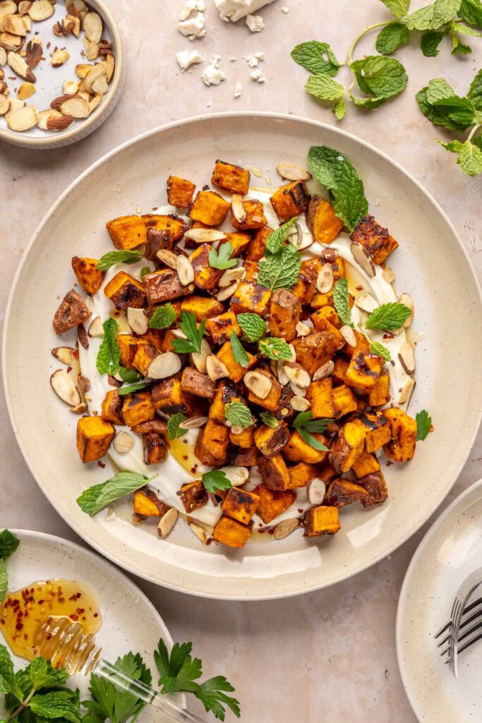 Plated roasted sweet potatoes over creamy whipped feta topped with hot honey, and fresh herbs