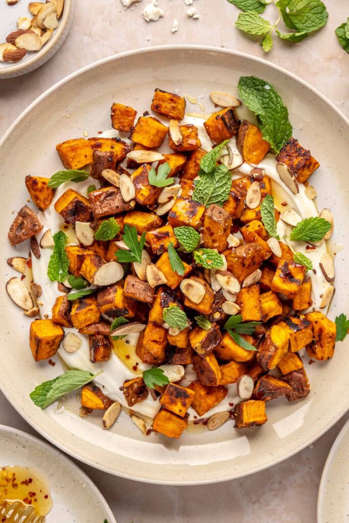 Plated roasted sweet potatoes over creamy whipped feta topped with hot honey, and fresh herbs