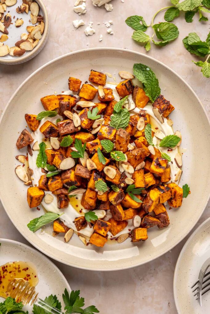 Plated roasted sweet potatoes over creamy whipped feta topped with hot honey, and fresh herbs