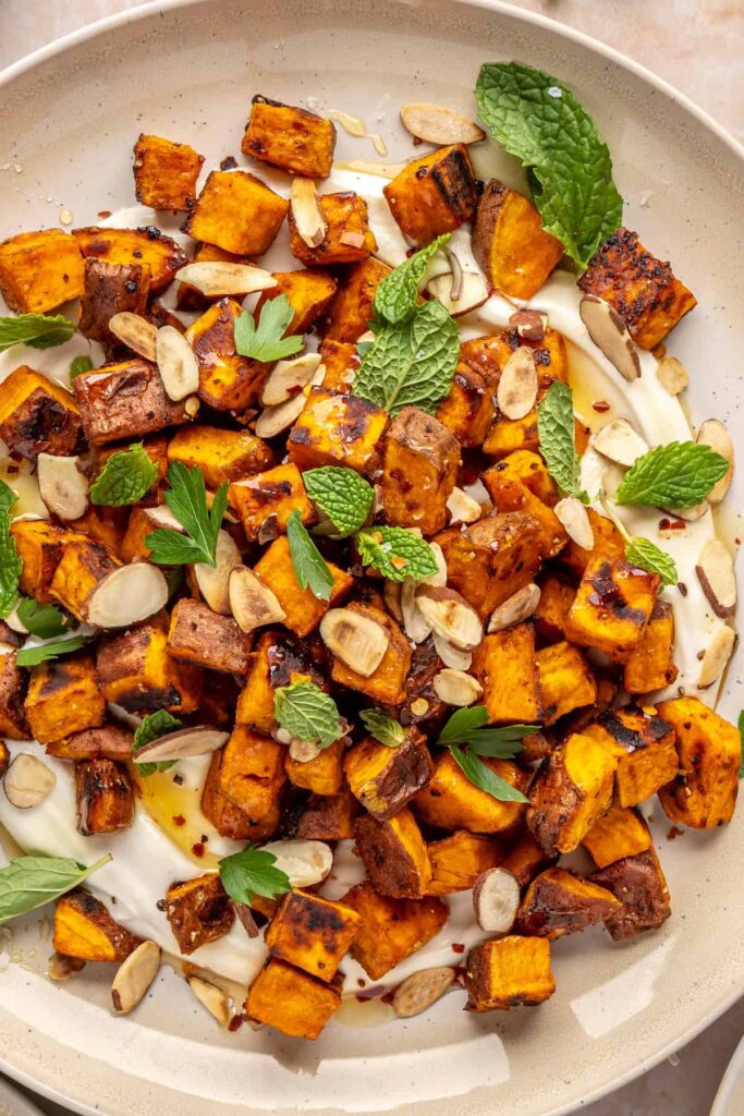Plated roasted sweet potatoes over creamy whipped feta topped with hot honey, and fresh herbs