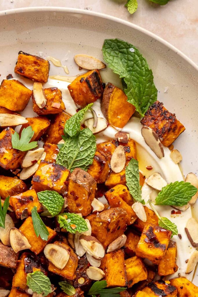 Plated roasted sweet potatoes over creamy whipped feta topped with hot honey, and fresh herbs