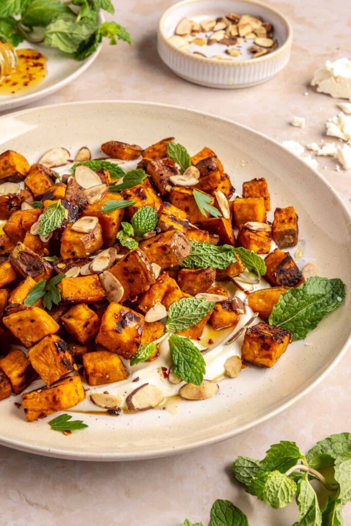 Plated roasted sweet potatoes over creamy whipped feta topped with hot honey, and fresh herbs