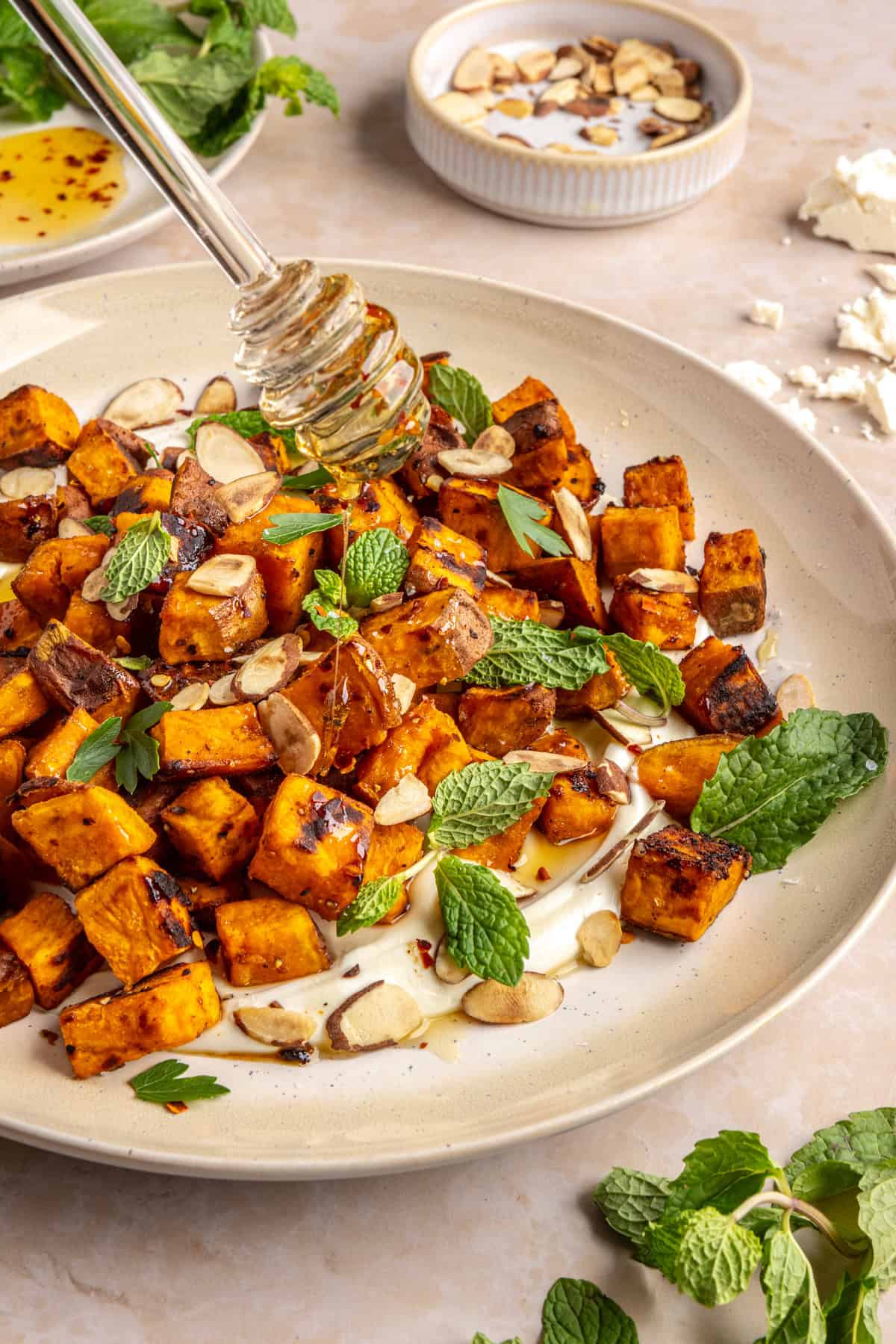 Drizzling hot honey over roasted sweet potatoes on a plate with whipped feta and toasted nuts