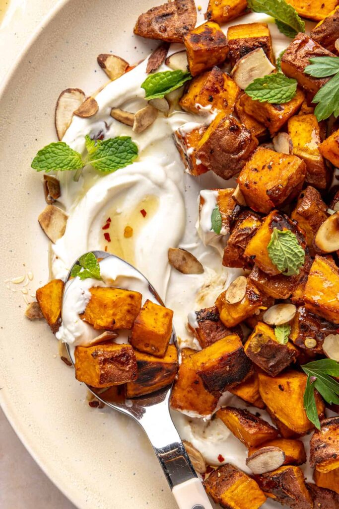 Crispy roasted sweet potatoes on a plate with whipped feta, hot honey, and toasted almonds