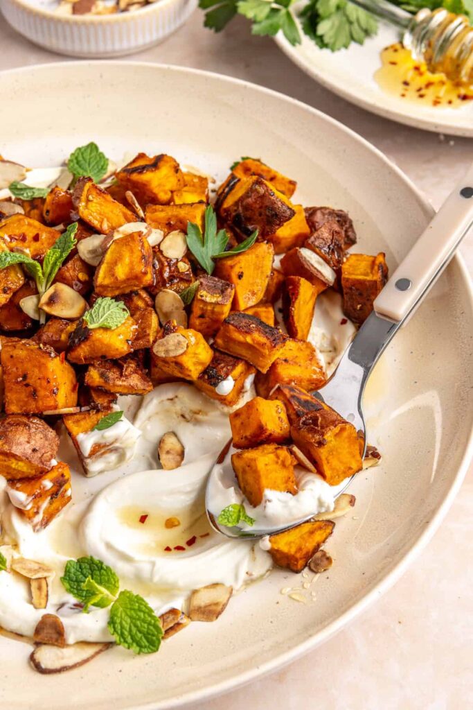 Crispy roasted sweet potatoes on a plate with whipped feta, hot honey, and toasted almonds