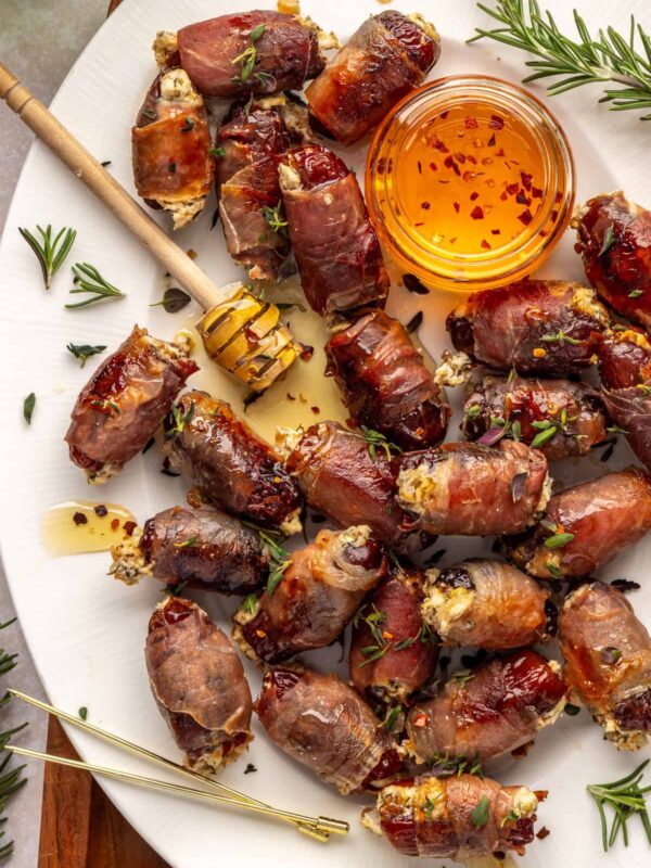 Holiday appetizer: prosciutto wrapped stuffed dates with goat cheese and hot honey on platter with honey dipper