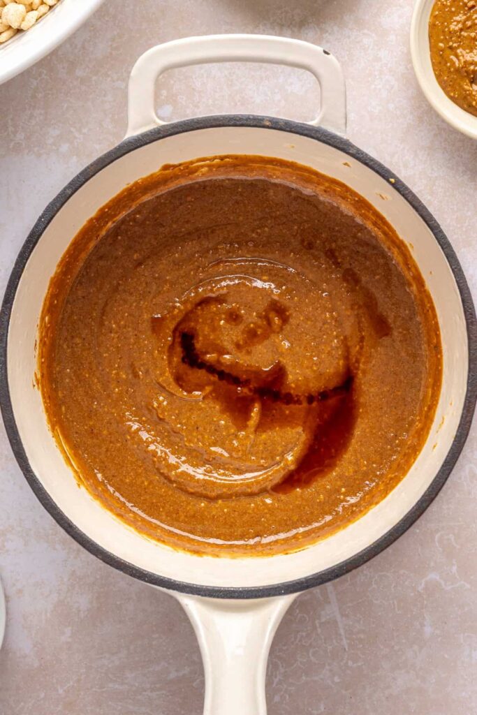 Melting peanut butter, maple syrup, coconut sugar, coconut oil, and salt in a pot for salted peanut butter bars.