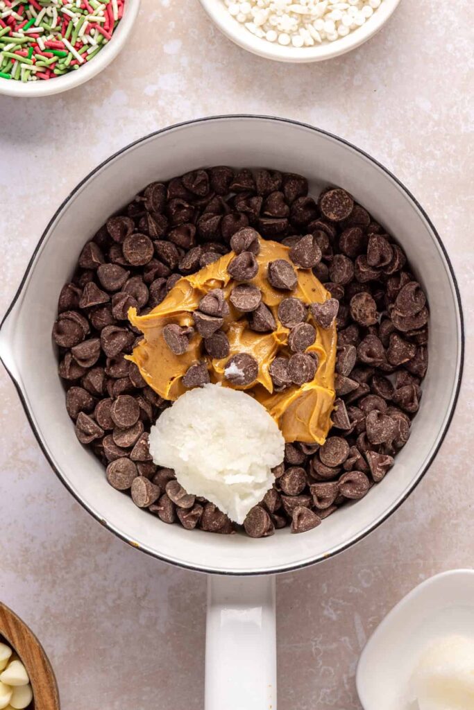 chocolate chips, peanut butter, and coconut oil in a pot, ready to be melted together for salted peanut butter bars topping.