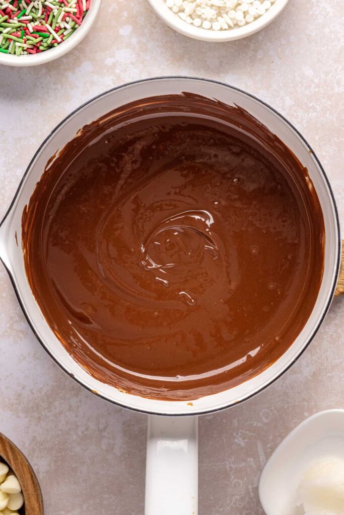 Melting chocolate chips, peanut butter, and coconut oil in a pot for salted peanut butter bars topping.