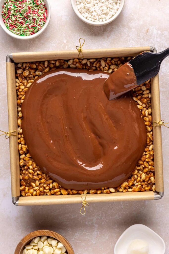 Pouring and spreading chocolate peanut butter topping over chilled salted peanut butter bars.