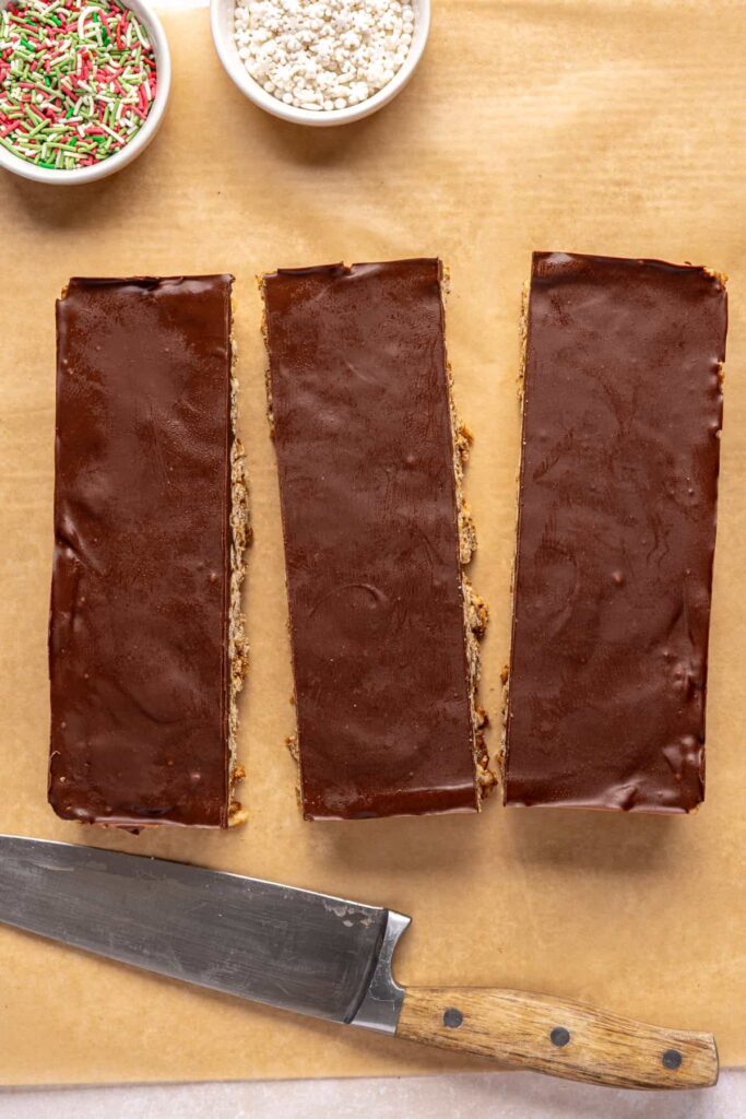 Cutting salted peanut butter bars into squares and triangles on a parchment-lined baking sheet.