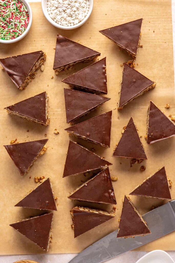 Cutting salted peanut butter bars into festive Christmas tree shapes on a parchment-lined baking sheet.