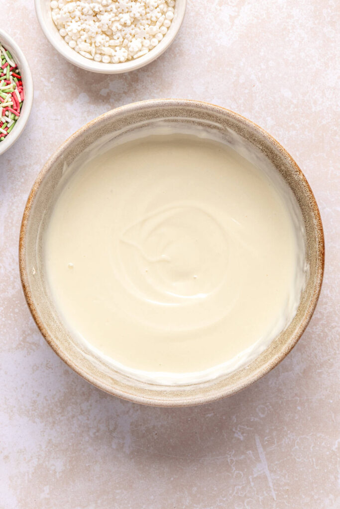 melted white chocolate chips and coconut oil in a bowl, ready to drizzle over Christmas tree-shaped salted peanut butter bars