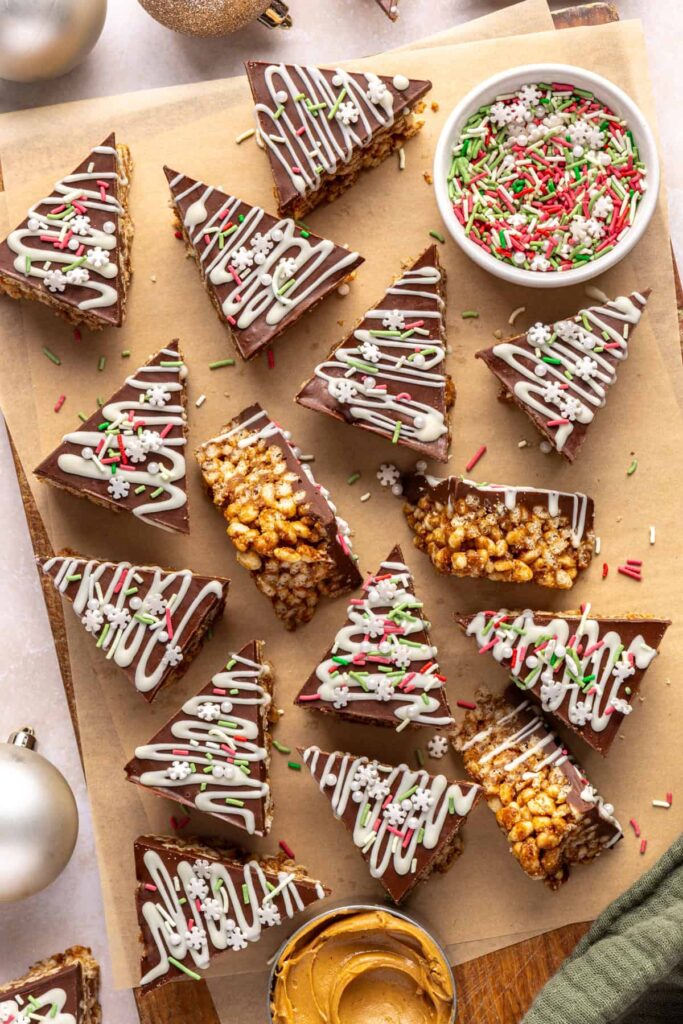 Finished salted peanut butter bars on a parchment-lined wooden board with a bowl of sprinkles and peanut butter nearby.