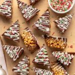 Finished salted peanut butter bars on a parchment-lined wooden board with a bowl of sprinkles and peanut butter nearby.