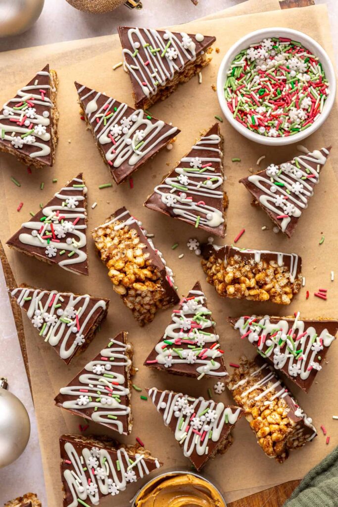 Finished salted peanut butter bars on a parchment-lined wooden board with a bowl of sprinkles and peanut butter nearby.