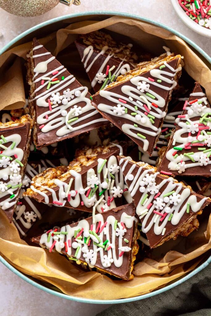 Homemade salted peanut butter bars in a holiday tin, topped with chocolate and white chocolate drizzle