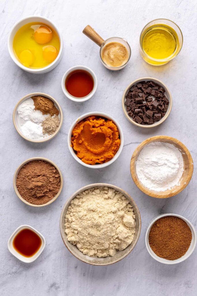 Overhead shot of ingredients for pumpkin spice chocolate loaf, including pumpkin puree, almond flour, cacao, and spices.