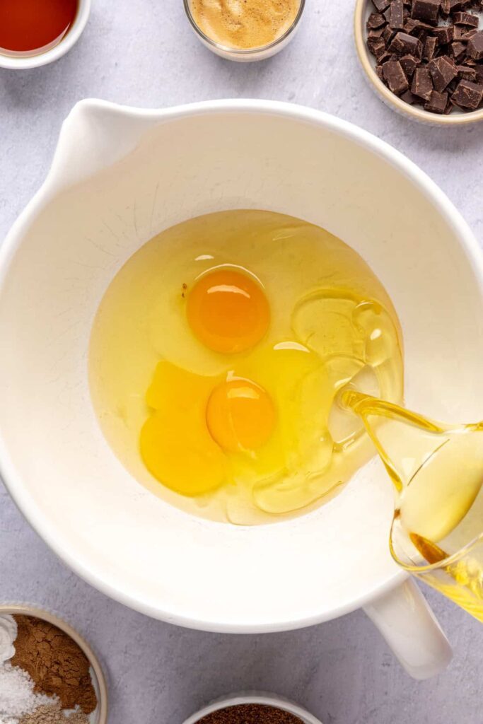 Pouring avocado oil into a bowl with eggs before mixing into a pumpkin spice chocolate loaf batter