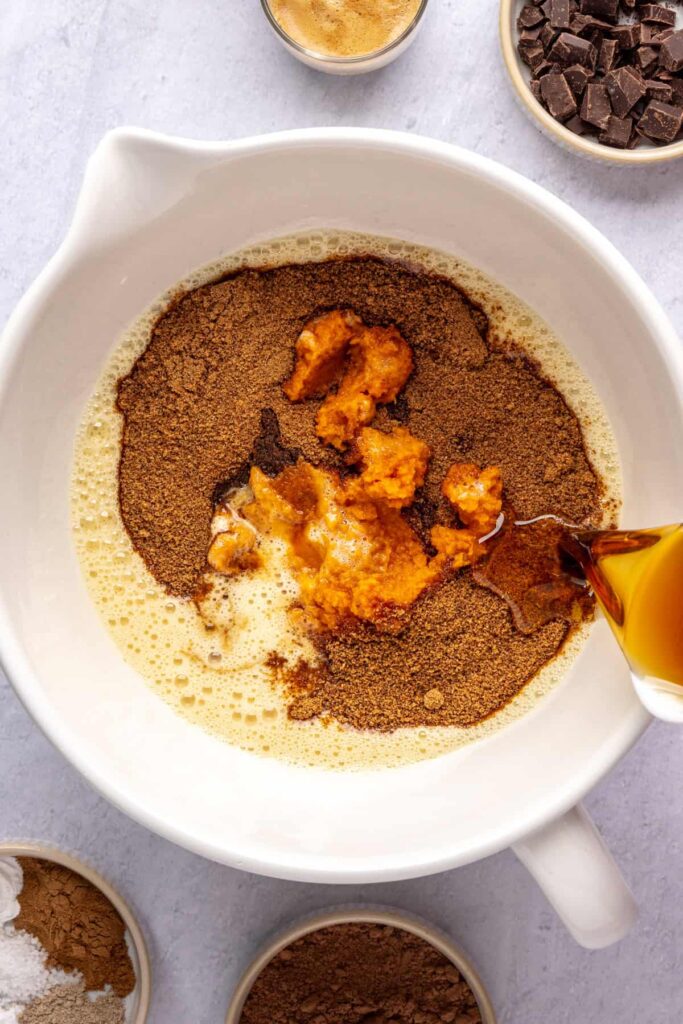 Wet ingredients—pumpkin puree, coconut sugar, maple syrup, and vanilla—in a bowl before being mixed for pumpkin spice chocolate loaf.