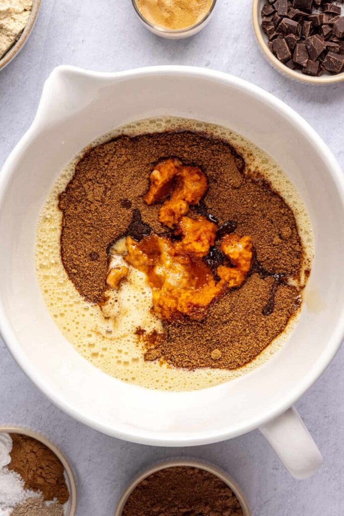 Wet ingredients—pumpkin puree, coconut sugar, maple syrup, and vanilla—in a bowl before being mixed for pumpkin spice chocolate loaf.