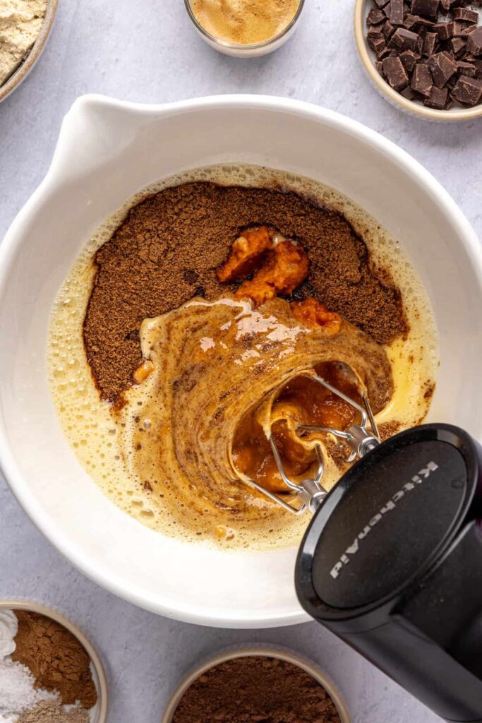 Wet ingredients—pumpkin puree, coconut sugar, maple syrup, and vanilla—being mixed for pumpkin spice chocolate loaf.