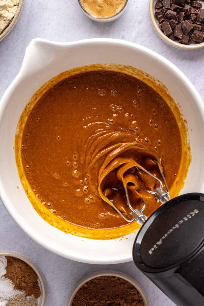 Wet ingredients—pumpkin puree, coconut sugar, maple syrup, and vanilla—being mixed for pumpkin spice chocolate loaf.